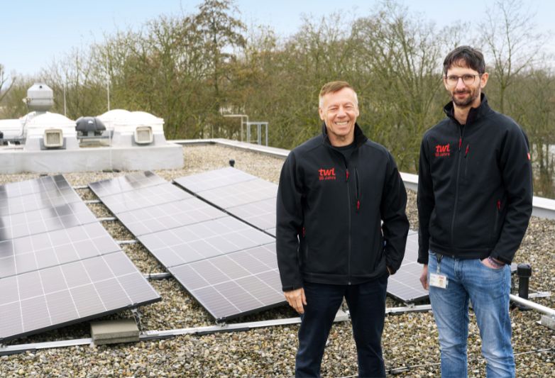 Zwei Kollegen stehen nebeneinander, im Hintergrund PV-Anlagen